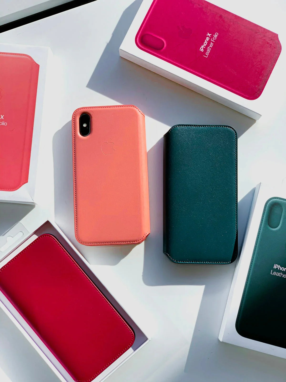 Renkli iPhone X deri kılıfları ve kutuları düz beyaz zeminde sergileniyor