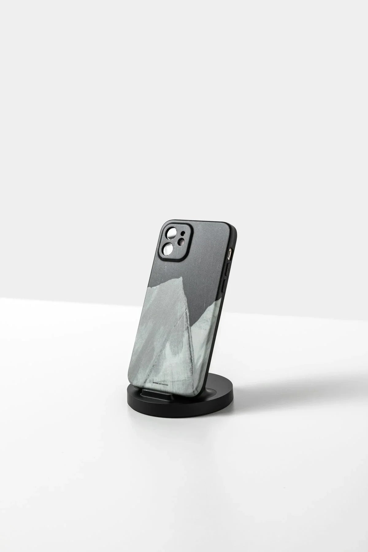 Siyah ve gri desenli iPhone kılıfı sade bir stand üzerinde, beyaz arka planda