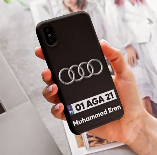 Kişiye özel isimli, plaka ve araba logolu siyah telefon kılıfı elde tutuluyor.